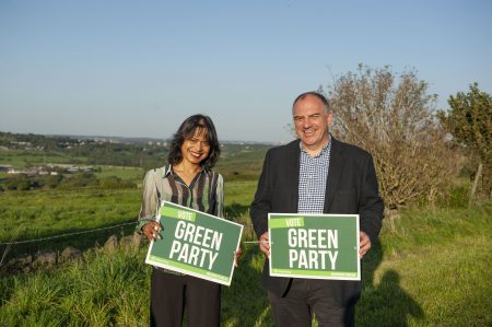 Andrew Cooper and Hawarun Hussain holding "Vote Green Party" boards in a field over looking the Tong Valley
