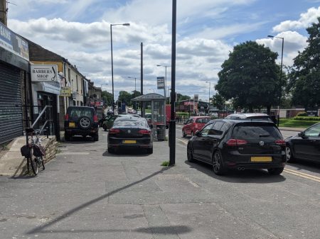 A number of cars parked dangerously on the pavement outside the shops on Tong Street