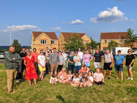 Councillor Matt Edwards and campaigner Celia Hickson stood with a large group of residents on grass land of Raikes Lane in Holmewood on a sunny day.