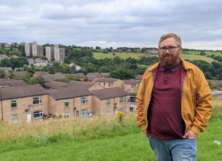 Matt Edwards standing with houses and blocks of flats of Holmewood in the background