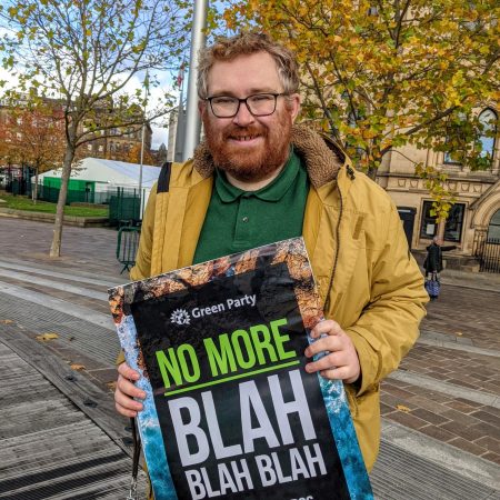 Councillor Matt Edwards holding a Green Party placard that says "No more Blah Blah Blah" in front of Bradford City Hall