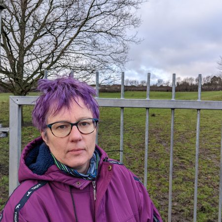 Celia Hickson stood in front of the former playing field at St. John's Primary School in Bierley. There is a large metal fence around the site.