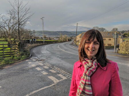 Councillor Caroline Whitaker standing next to a road with a view of Silsden in the background