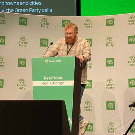 a photograph of Matt Edwards at the podium on the stage at Green Party conference